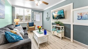 Un salon avec un ventilateur de plafond, un téléviseur, un canapé, une table basse et une bibliothèque.
