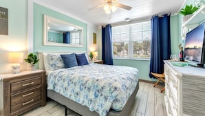 Une chambre à coucher comprenant un lit, une table de chevet, une commode, un miroir et une fenêtre avec des rideaux.