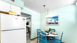 Une cuisine avec un réfrigérateur blanc, des chaises bleues, une table à manger et un luminaire suspendu.