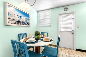 Un comedor con una mesa redonda, sillas azules, un cuadro enmarcado y una puerta con un reloj.