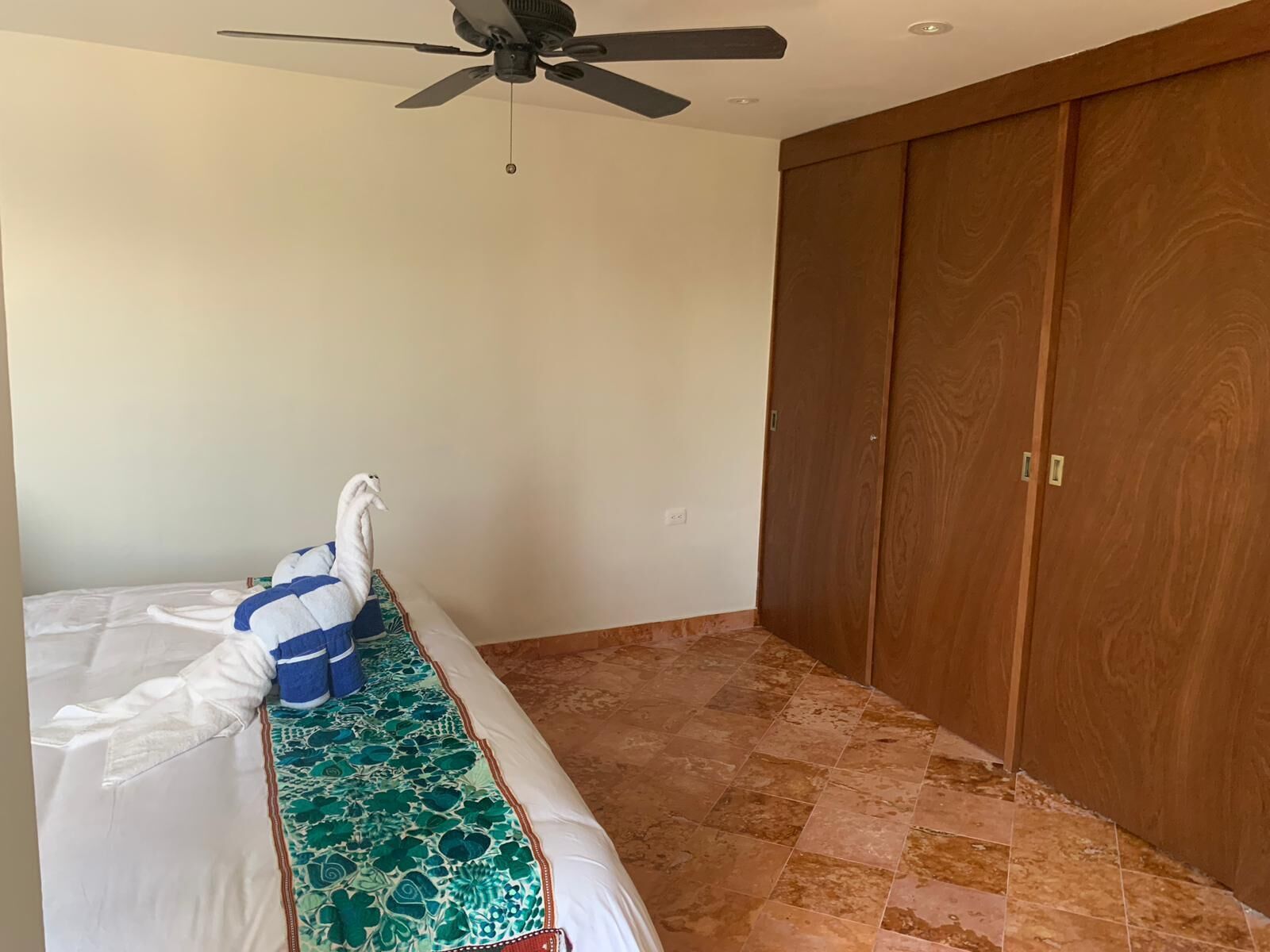 A bedroom with a bed, a ceiling fan, and a wooden wardrobe.