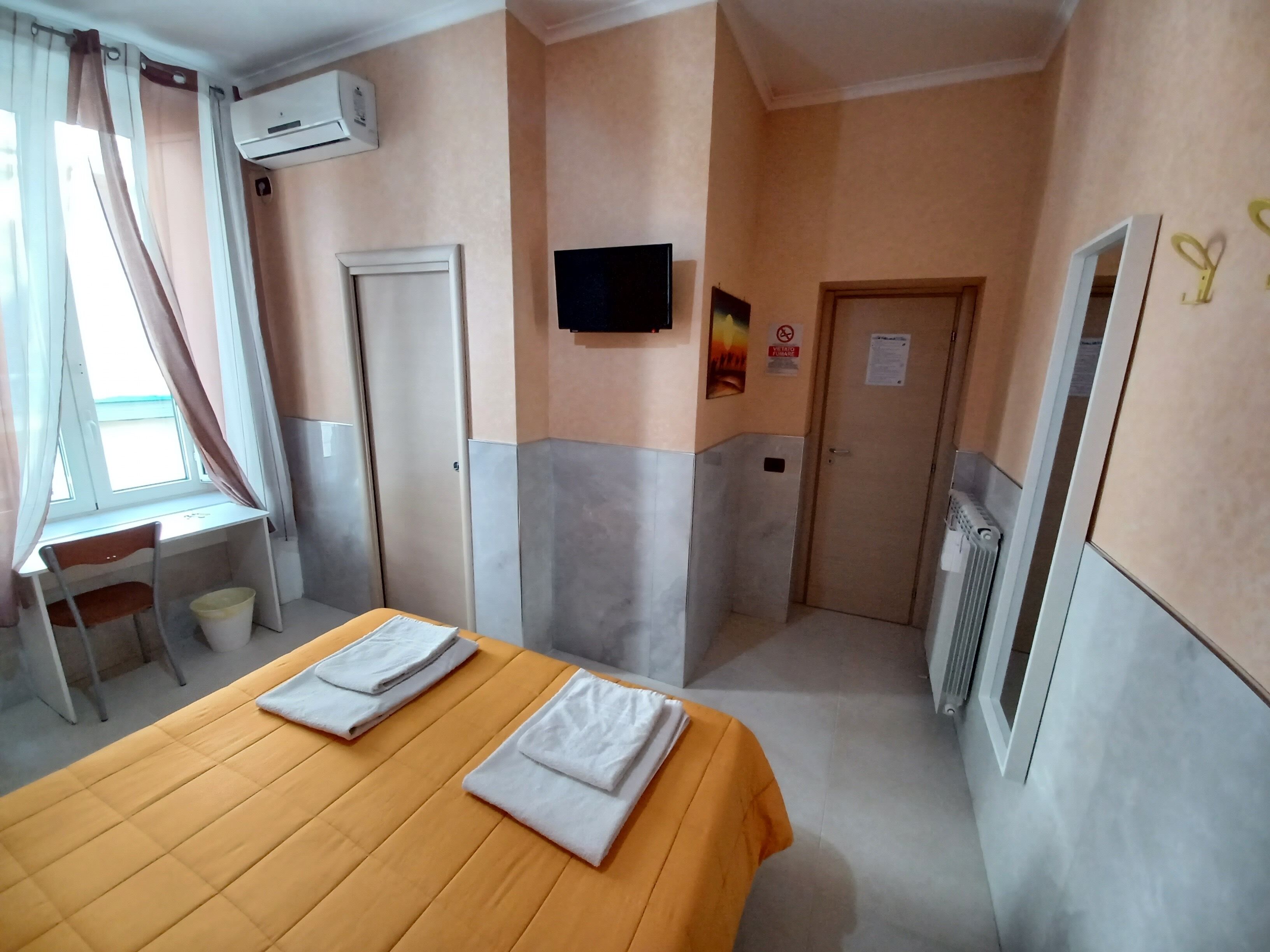 A hotel room with a bed, a desk, an air conditioning unit, a TV, and a door.