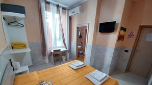 A hotel room with a bed, a desk, a chair, a small table, a shelf with a towel, and an air conditioning unit. - B&B Quattro Palazzi center of Naples, in the heart of Naples. (Napoli)