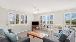 A living room with a TV, sofa, coffee table, and a dining area with chairs and a table.