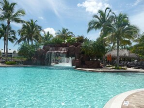A clear pool with a waterfall feature, surrounded by palm trees and lounge chairs. - Beautiful Condo in Tranquil, Tropical Setting in Flamingo Fairways 2 (Naples)