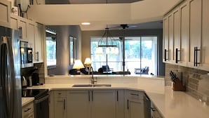 A modern kitchen with a large island, stainless steel appliances, and a view to the outside. - Beautiful Condo in Tranquil, Tropical Setting in Flamingo Fairways 2 (Naples)