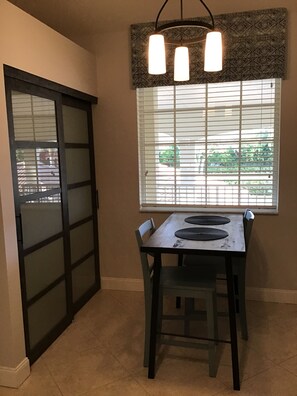 A dining area with a table and chairs, a patterned window valance, and a sliding door. - Beautiful Condo in Tranquil, Tropical Setting in Flamingo Fairways 2 (Naples)