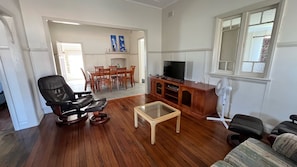 A living room with a black leather chair, a wooden coffee table, a TV stand, and a dining area with wooden chairs and a table.