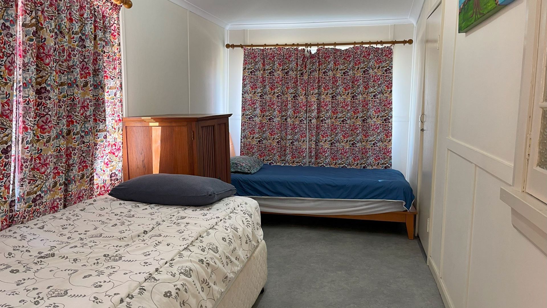 A bedroom with a bed, a wooden wardrobe, and floral curtains.