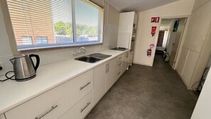 A compact kitchen with a kettle, sink, and cabinets. - EAGLETON COTTAGE - 5 MINUTE WALK TO THE BEACH. (South West Rocks)
