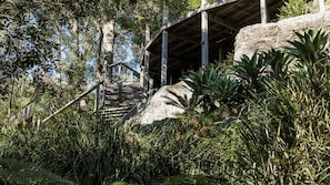 Una escalera de madera que conduce a un edificio de piedra rodeado de abundante vegetación.