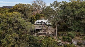 Uma casa rodeada por floresta densa, com uma escadaria de pedra que a conduz.