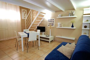 A modern living room with a blue sofa, white dining table, and chairs. A staircase with a white railing leads to an upper level. - Virna House in Castellammare del Golfo (Scopello)