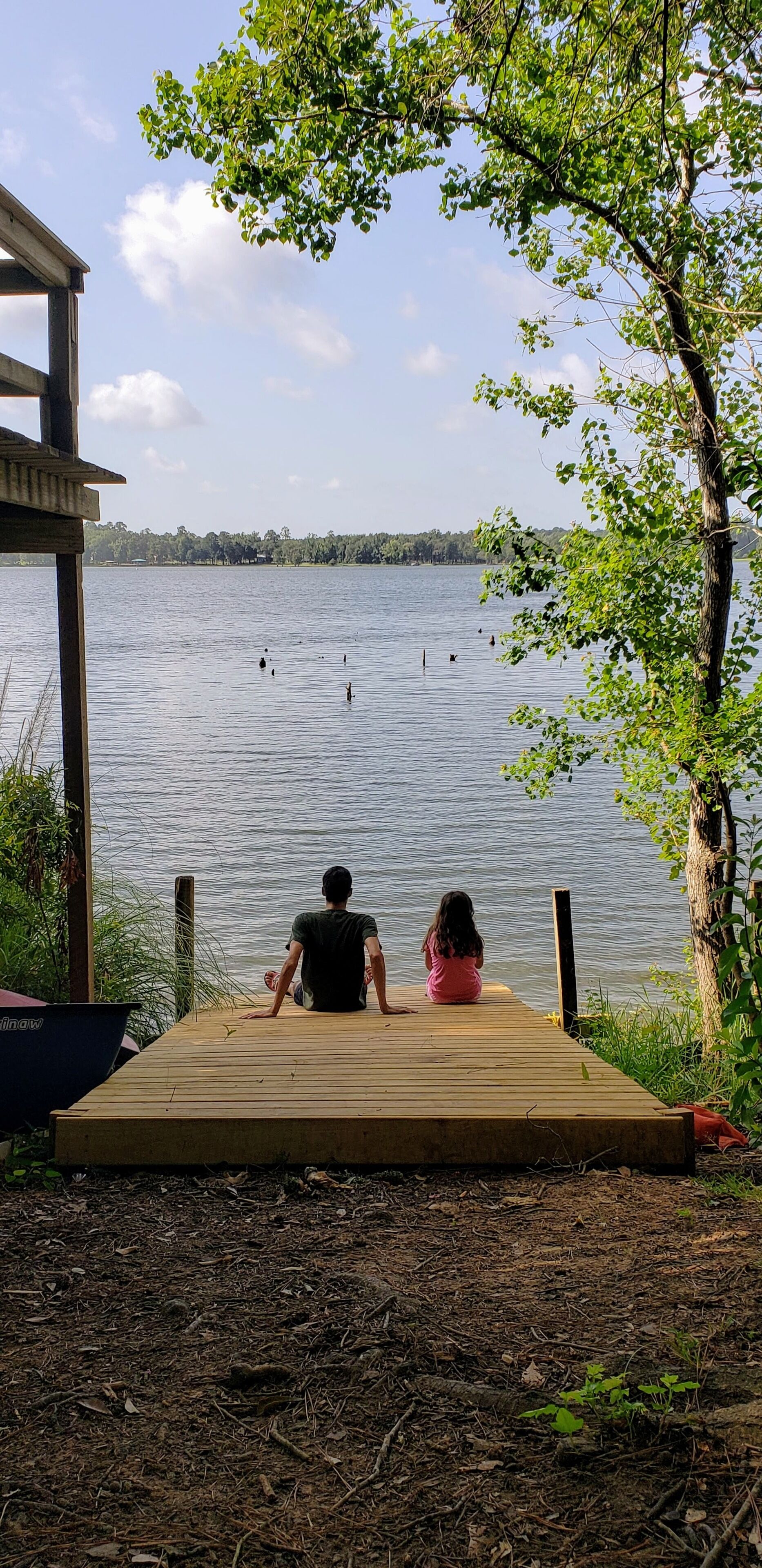 A wooden dock extending into a lake with two people sitting at the end.