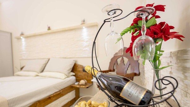 Une chambre à coucher avec un lit, une table de chevet sur laquelle se trouve une bouteille de champagne, un bol de collations et un vase décoratif rempli de fleurs.