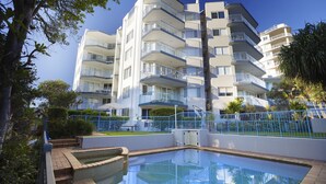 Un immeuble résidentiel à plusieurs étages, doté de balcons, d’une piscine et entouré de verdure.