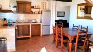 Una cocina con armarios de madera, salpicadero de azulejos, un refrigerador y una mesa de comedor con sillas.