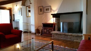 Una sala de estar con chimenea, sillones rojos, una mesa de centro de vidrio y una mesita auxiliar de metal.