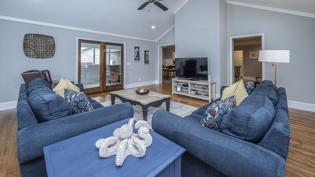 Ein Wohnzimmer mit zwei blauen Sofas, einem Couchtisch mit einer Dekoration, einem Deckenventilator, einem Fernseher und einer Lampe.