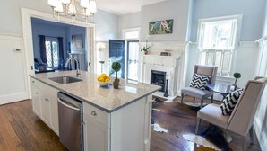 A spacious kitchen with a central island, a dining area with a fireplace, and a living room with a large window. - Chic Bohemian Two-Story Home w/ Courtyard & Parking by Lucky Savannah (Savannah)