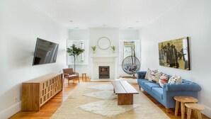 A modern living room with a blue sofa, wooden coffee table, and a TV mounted on the wall. - Chic Bohemian Two-Story Home w/ Courtyard & Parking by Lucky Savannah (Savannah)