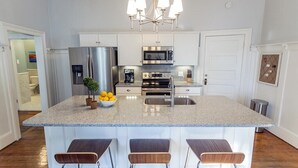 A modern kitchen with a granite countertop, stainless steel appliances, and a bar area with stools. - Chic Bohemian Two-Story Home w/ Courtyard & Parking by Lucky Savannah (Savannah)