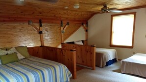 Un dormitorio acogedor en el ático, con techo inclinado de madera, un ventanal grande y dos camas individuales.