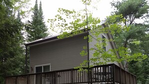 Una casa de dos pisos con una terraza de madera, rodeada de árboles.