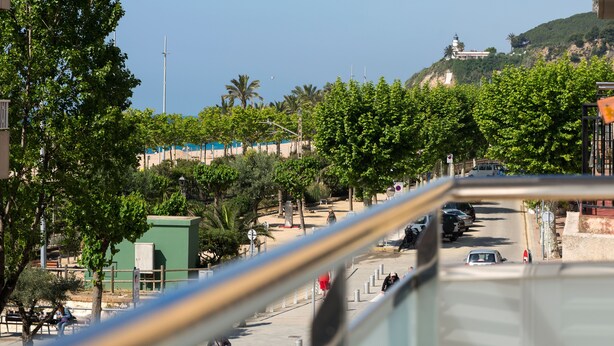 A coastal street with parked cars, trees, and a hill with a lighthouse. - Beach Apartment in Calella, Barcelona. Free Wifi, a / c (Calella)