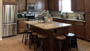 A modern kitchen with wooden cabinets, stainless steel appliances, and a central island with bar stools. - Escape the heat and cool off this summer in the Guadalupe! (New Braunfels)