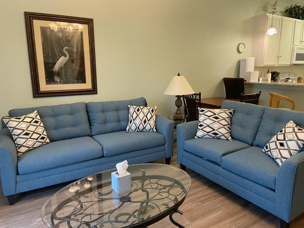 A living room with two blue sofas, a glass coffee table, and a framed picture on the wall.