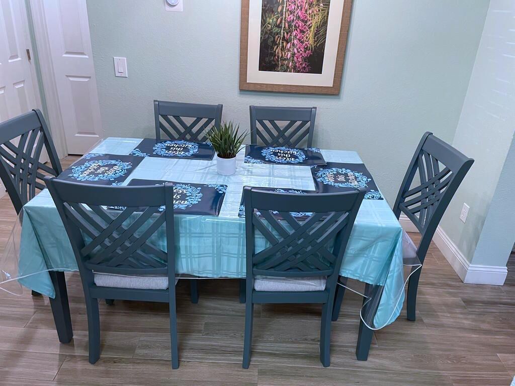 A dining table set with chairs, a small plant, and a framed picture on the wall.