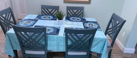 A dining table set with chairs, a small plant, and a framed picture on the wall.