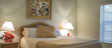 Una cama bien hecha con una colcha color beige y almohadones, flanqueada por dos mesitas de noche con lámparas. Encima de la cama, un cuadro enmarcado con motivos florales.
