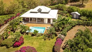 Une grande maison avec une piscine, entourée de jardins luxuriants et d’arbres.