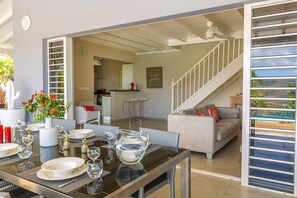 Un coin repas avec une table en verre dressée pour un repas, un canapé et un escalier menant à un autre niveau.