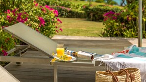 Een houten terras met een glazen tafel gedekt voor het ontbijt, inclusief een krant, een glas sinaasappelsap en een mand.