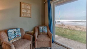 Una habitación con dos sillones, una mesita y un ventanal con vista a una playa y una valla.