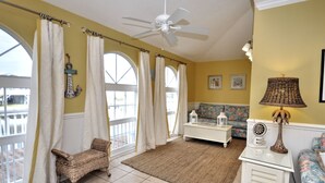 Un salon spacieux doté d’un grand ventilateur de plafond, de larges fenêtres avec des rideaux, d’un canapé, d’une table basse et d’une lampe décorative.