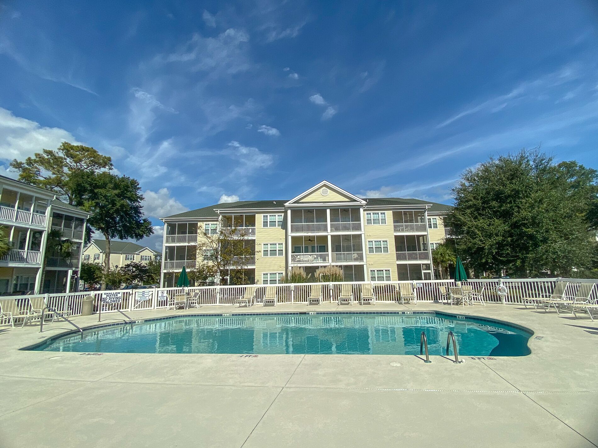 A pool area with a pool, lounge chairs, and a building with multiple balconies.