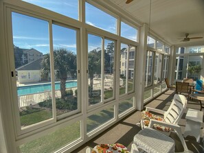 A sunroom with large windows overlooking a backyard with a pool and palm trees.