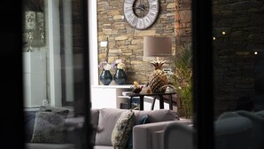 A living room with a stone wall, a round clock, a table with a lamp, and a sofa with cushions. - Longra Family Villa & SPA (Mirandela)