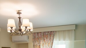 A hotel room with a bed, a nightstand, a lamp, a mirror, and a window with curtains. - Villa Nina (Penteli)