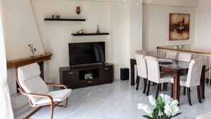 A modern living room with a flat-screen TV, a glass-top dining table with chairs, a wooden entertainment unit, and a chandelier. - Villa Nina (Penteli)