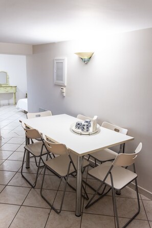 A dining area with a white table and four chairs, a small table with a decorative item, and a wall-mounted light fixture. - Villa Nina (Penteli)