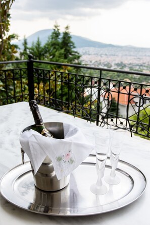 A terrace with a metal tray holding a champagne bottle and two glasses, set against a scenic mountain backdrop. - Villa Nina (Penteli)