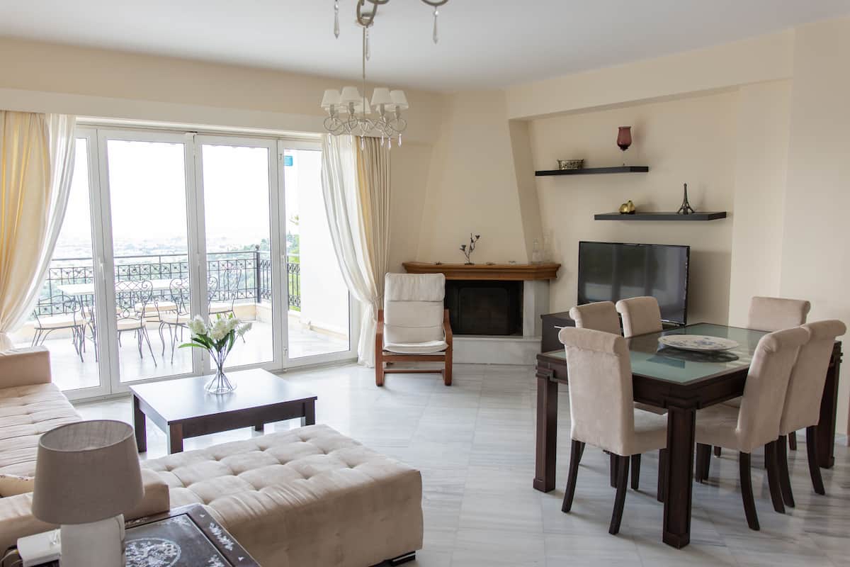 A spacious living room with a balcony, a fireplace, a dining table with chairs, and a television.