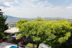 Une terrasse avec une piscine, du mobilier d’extérieur et une vue sur le paysage urbain et les montagnes.