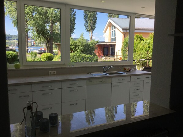 A kitchen with a large window, white cabinets, and a stainless steel sink. - Apartment Anker am See (Wangen)