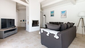 A living room with a grey sofa, a TV, a fireplace, and two framed pictures on the wall.